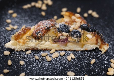 sprinkle with powdered sugar delicious pie with pear and Brit cheese curd cheesecake nuts almonds and cashews on black snow-covered plate with sugar delicious appetizing dessert serving blueberries