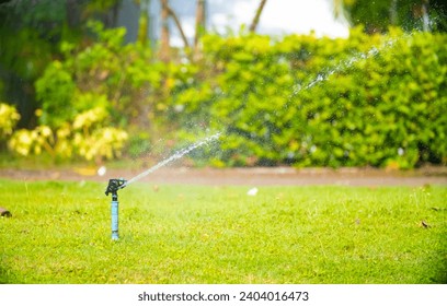 Sprinkler for automatic lawn watering. Lawn cultivation and care, garden irrigation devices. Rainbow over the garden on a sunny day. - Powered by Shutterstock