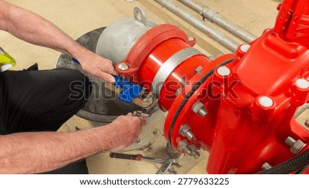 Sprinkler engineer checking water supply pump on a red valve set for a sprinkler fire protection system. Close up of engineers hands working on a sprinkler fire suppression system. Industrial fire prevention equipment.