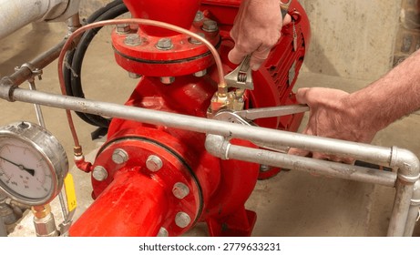 Sprinkler engineer replacing a valve on a red pump set using spanners during maintenance of an industrial fire protection system.