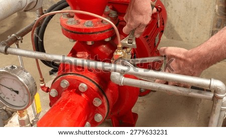 Sprinkler engineer replacing a valve on a red pump set using spanners during maintenance of an industrial fire protection system.