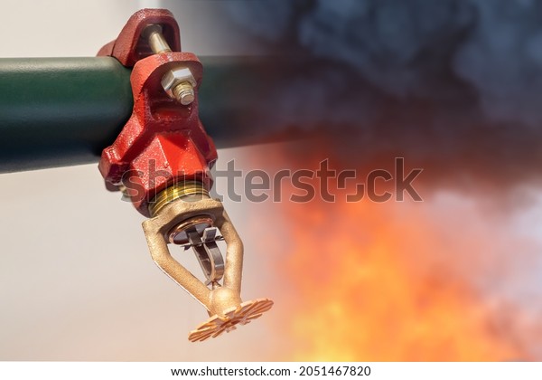 Sprinkler for fire extinguishing system.\
Sprinkler next to flame and smoke. Concept - equipment for fire\
fighting. Sprinkler for extinguishing flame in building. Internal\
fire extinguishing\
system.