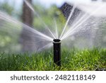 Sprinkler spraying water on green grass in garden. Irrigation system