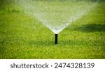 Sprinkler system watering a lush green lawn on a sunny day.