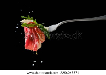 Sprinkling piece of marbled beef carpaccio on fork with lemon juice over black background