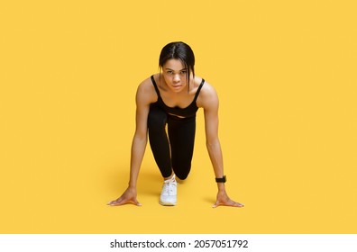 Sprint concept. Young african american female athlete in starting position ready for running looking at camera, exercising over yellow studio background, copy space