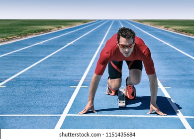 Sprinter Athlete Ready To Start Running Race Waiting At Line On Starting Blocks On Blue Run Tracks At Outdoor Stadium. Focus And Motivation Sport And Fitness Concept.