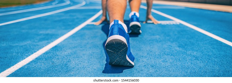 Sprinter fit man waiting for start of race on running tracks at outdoor stadium. Sport and fitness runner athlete on blue run track starting line with running shoes. Banner panorama.