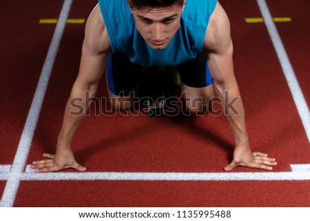 Sprinter leaving starting blocks on the running track in front of big modern stadium with lights. Explosive start.
