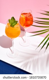 Spritz-Cocktail auf weißem Tisch. Tropischer Schatten aus Palmenblättern. Sommercocktailgruppe. Rosa und klassisch-blauer Hintergrund