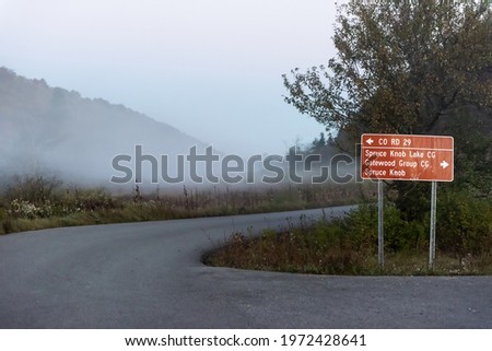 Spruce Knob Lake road in West Virginia in morning with sign directions and mist fog frost and forest trees in autumn fall season landscape view