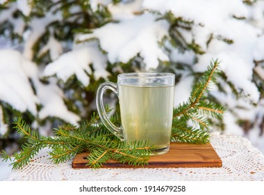 Spruce tree needle tea infusion in transparent glass tea cup. Snowy blurred spruce tree on background, outdoors on cold winter day. Room for text.