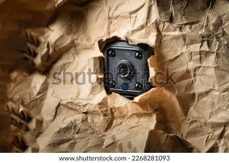 A spy camera hide in torn paper hole . Hidden camera or detective or scandal concept.