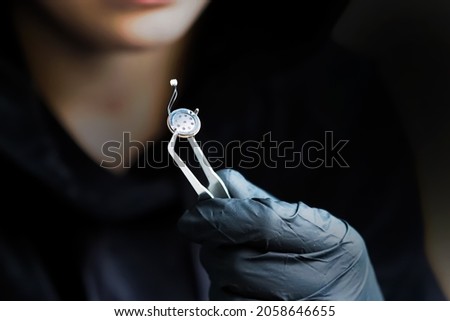 Spy games. Small microphone of the overhearing device, spy holding a microphone with tweezers, black gloves. Micro listening device