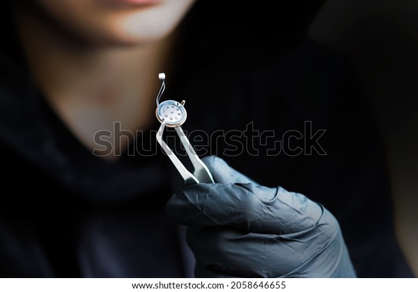 Spy games. Small microphone of the overhearing
device, spy holding a microphone with tweezers, black gloves. Micro
listening device