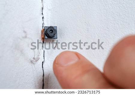 Spy hidden camera in the crack of the wall. Man discovers micro camera in office. Spy scandal, collecting compromising evidence, wiretapping, symbolic image.