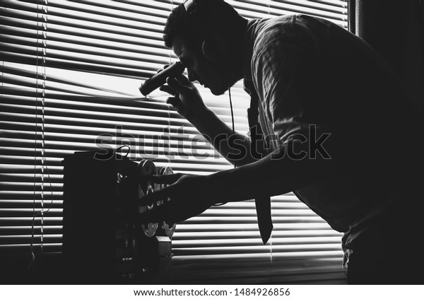 Spying through the window. Special agent listens\
on the reel tape recorder. Officer wiretapping with flashlight in\
hands. Old shutter\
blinds.