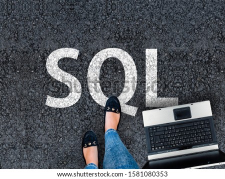 Sql programming language. A woman steps to a laptop and sql on asphalt. Structured Query Language road