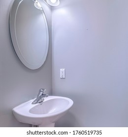 Square Bathroom Interior With Wall Light And Oval Mirror Over Stand Alone Pedestal Sink