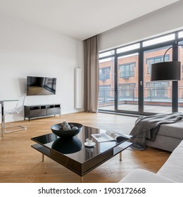 Square, Black Coffee Table In Spacious Living Room With Television Screen And Big Window Doors To Balcony