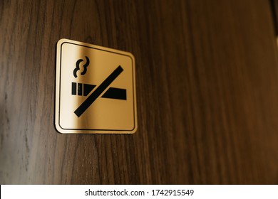 Square Black And Golden Metallic No Smoking Sign On A Brown Wooden Door Inside A Hotel Room. Non-smoking Space For Incription Sign On Metal Texture Crossed Cigarette Smoke. Selective Focus