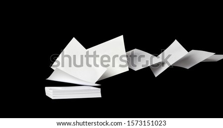 Square blank white papers flying away from a stack in the wind, on black
