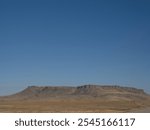 Square Butte, near Fort Shaw, Montana, with blue sky that is common in Big Sky Country. A small herd of cattle is grazing in the background and a gravel road is winding toward the mountain.