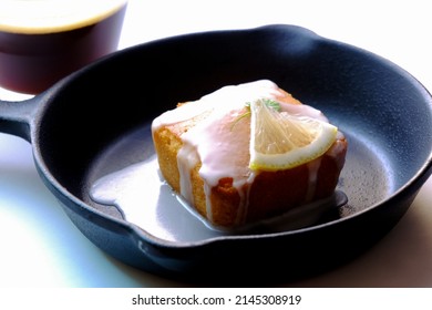 The Square Cake With Black Coffee Cup. It Has White Sauce On Metal Pan And Has Lemon On Top