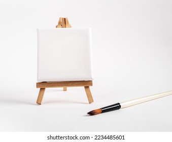 Square canvas on tiny mini easel, blank mockup on wood tripod, paintbrush. Artistic supplies composition. High quality photo - Powered by Shutterstock