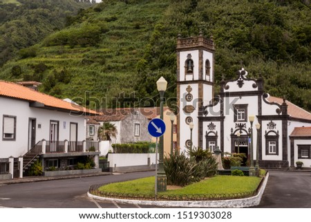 Square devided by grass island with a traffic sign, surrounded by houses. Typical portuguese white church. Forest on a hill in the background. Faial da Terra, Sao Miguel, Azores Islands, Portugal.