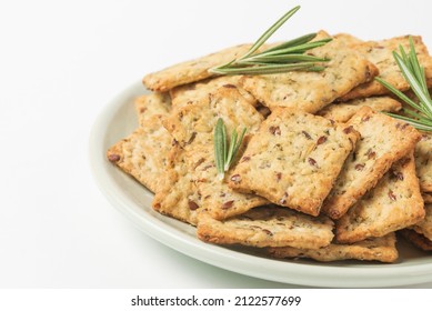 Square diet cookies with rosemary, flax seeds and spices  in a light plate on white background. Crunchy herbal crackers close up plan with low depth of field