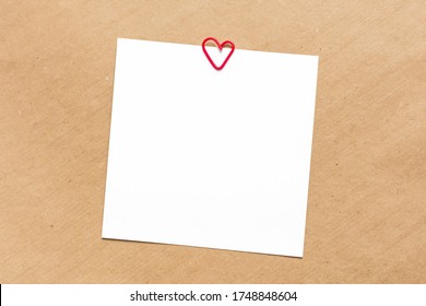 Square empty white sheets on kraft paper background. Red paper clip in the shape of a heart. Top view