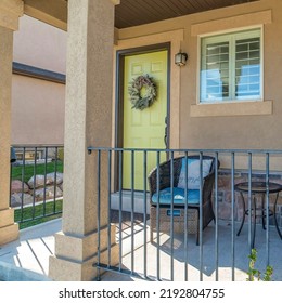 Square Exterior Of A Porch Of A House With Woven Lounge Seats And Metal Railings. House Exterior With Light Green Door With Wreath Near The Windows And A Stone Veneer Siding.