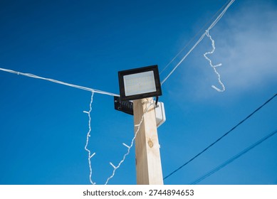 Square Floodlight And Festive String Lights Intersecting Against Deep Blue Sky, Twisting Cables And Sharp Silhouettes, Highangle Composition, Celebratory Mood And Eventready Atmosphere