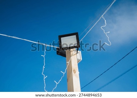Square Floodlight And Festive String Lights Intersecting Against Deep Blue Sky, Twisting Cables And Sharp Silhouettes, Highangle Composition, Celebratory Mood And Eventready Atmosphere