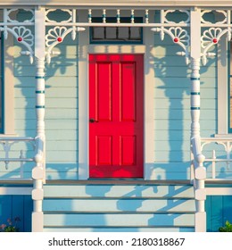 Square Front Porch Exterior With Red Front Door At Oceanside, California. Porch With White Railings And Posts Against The Light Blue Wooden Wall Sidings.