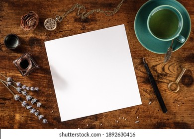A square greeting card or invitation design mock-up, shot from the top on a dark rustic wooden background with lavender and tea