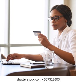 Square Image Of Beautiful Young Black Female Busy Holding A Credit Card In One Hand Reading Off The Required Information And Typing In The Relevant Digits To Make Payments For Her Online Shopping.