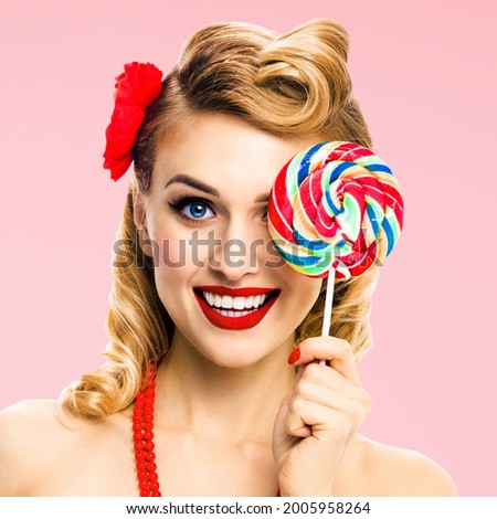 Square image - half face portrait of excited blond woman with lollipop covering one eye. Pin up girl with happy smile. Retro style. Rose pink colour back. Ophthalmology concept.