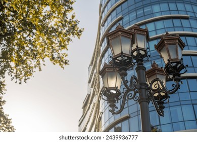 Square lantern before a multi-story office, with a tree silhouette and dusk sky, blending utility and aesthetics