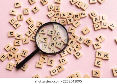 Square letter tiles with magnifying glass against pink background. Search for words and information concept.