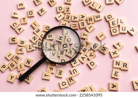 Square letter tiles with magnifying glass against pink background. Search for words and information concept.