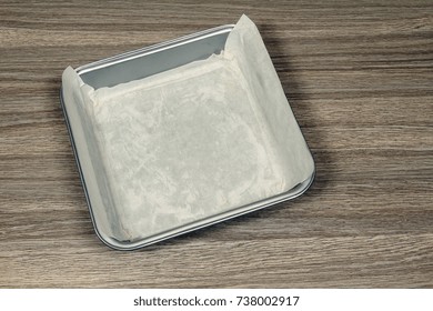 A Square Metallic Baking Tray Lined With Baking Paper On A Wooden Kitchen Counter.