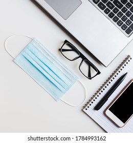 Square Office Flat Lay: Laptop, Reading Glasses, Smartphone, Pen, Note Pad And Medical Face Mask On White Desk. New Normal During Covid 19 Pandemic