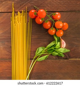 A square overhead photo of a letter P for pasta, formed by spaghetti, cherry tomatoes, a garlic clove, and a sprig of basil leaves, on a dark wooden background texture with copy space