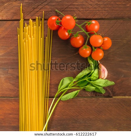 A square overhead photo of a letter P for pasta, formed by spaghetti, cherry tomatoes, a garlic clove, and a sprig of basil leaves, on a dark wooden background texture with copy space