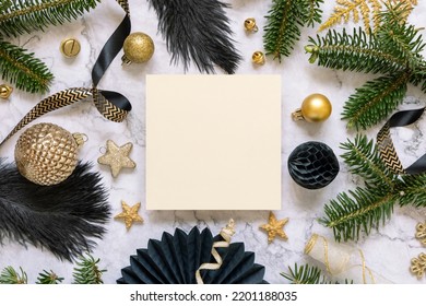 Square Paper Card Between Black And Golden Christmas Decorations And Fir Tree Branches Top View. Winter Composition With Blank Invitation Card Mockup, Copy Space