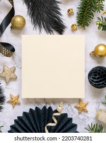 Square Paper Card Between Black And Golden Christmas Decorations And Fir Tree Branches Top View. Winter Composition With Blank Invitation Card Mockup, Copy Space