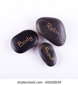 Square Photo Of Three Lava Stones. Black Stones With Words Relax, Body And Soul. Stones For Relaxing Massage Placed On White Board. Words Written By Gold Color On Black Stones.