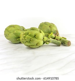 A square photo of three vibrant artichokes on a white marble texture with copy space